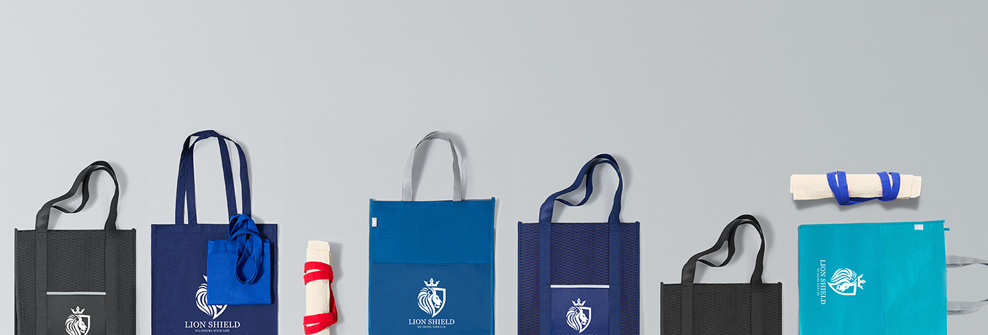 A variety of  branded bags and promotional bags layed out on display from blue messenger bags, backpacks, and tote bags with straps.
